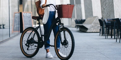 Person steht mit einem Fahrrad in der Stadt, dass einen Fahrradkorb vorne hat.