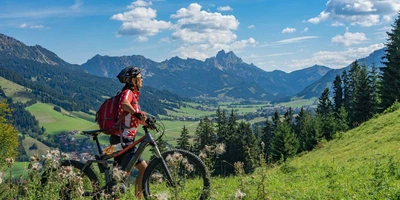 Ist das Light-E-MTB der neue Mega Trend 2024? Frau schiebt E-Mountainbike durch die Berge