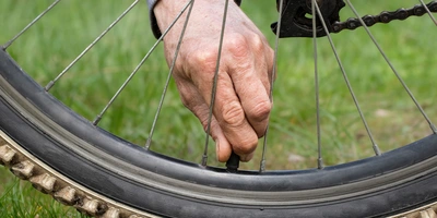 Nahaufnahme von einem Fahrradreifen mit einem Ventil, an dem eine Person anfässt.