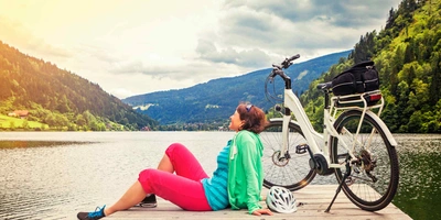 Frau sitzt neben E-Bike an See.