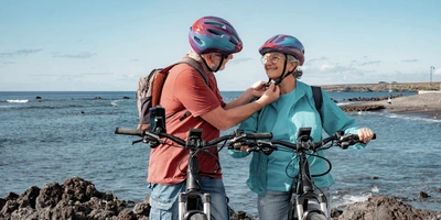 Älterer Herr macht den Fahrradhelm von Frau zu.