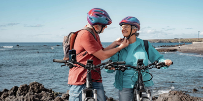 Das sind die innovativen Features der Advanced E-Bikes. Älterer Herr macht den Fahrradhelm von Frau zu.