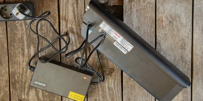 E-Bike Akkus – diese Alternativen gibt es. Foto von E-Bike Akku und Ladegerät mit Holzuntergrund.