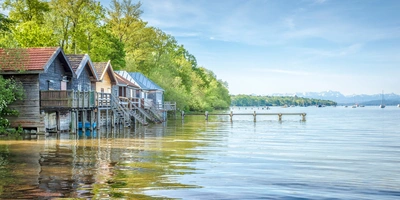 Ammersee Radweg: Die schönsten Radtouren rund um den See Blick auf ein ruhiges Gewässer mit Holzhäusern und grünen Bäumen im Hintergrund.