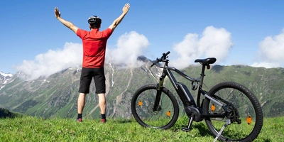 Person steht neben einem E-Bike auf einer grünen Wiese