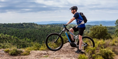 Erkunde abenteuerliche Trails mit der 5. Generation des Bosch CX-Motors Mann auf einem E-Mountainbike steht auf der Spitze eines Berges.
