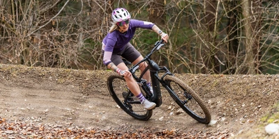 corratec E-Bike Test Mountainbikerin fährt mit Schwung eine kurvige Strecke im Wald.