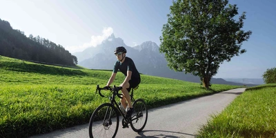 Mann fährt auf Crossbike über eine Straße zwischen einer Wiese her.