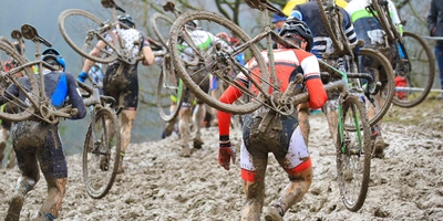 Radsportler laufen durch Schlamm mit ihren Fahrrädern