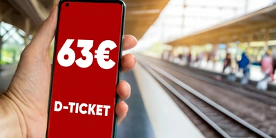 Deutschlandticket für 63€ Hand hält ein Smartphone mit einem D-Ticket und Preisangabe am Bahnhof.