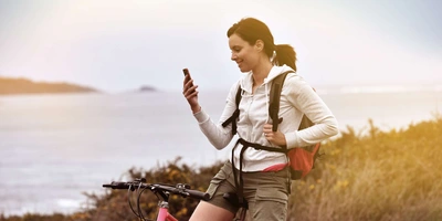 Sportlich gekleidete Frau auf Fahrrad in der Natur schaut auf Smartphone