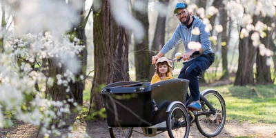 Person fährt Kinder in einem Lastenrad durch den Park