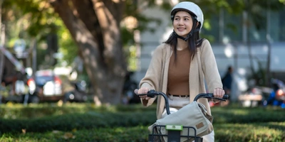 Junge Frau mit Helm auf einem Fahrrad in einem Park, lächelt zufrieden.
