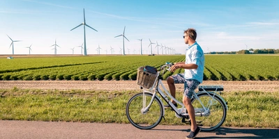 Junger Mann steht auf einem Fahrrad neben Windrädern und blickt auf die Felder
