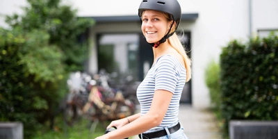 E-Scooter Helmpflicht – das musst du wissen Junge Frau mit Helm steht neben einem E-Scooter vor einem Wohnhaus