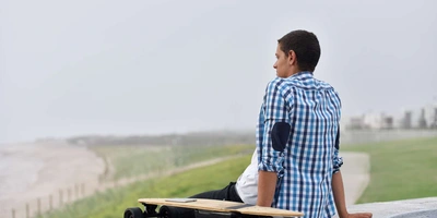 Mann sitzt auf dem Boden und neben ihm steht ein E-Skateboard