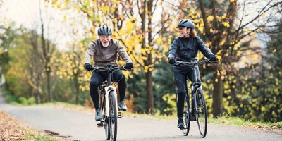 Älterer Mann und ältere Frau fahren Fahrrad und lächeln.