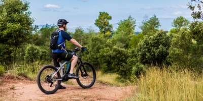 Mann auf E-Bike fährt durch Landschaft.