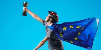 Mann auf Fahrrad mit Helm hält Pokal in die Luft.