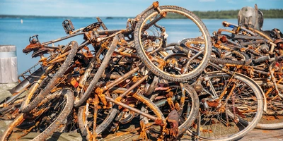 Ein Haufen rostiger Fahrradrahmen und Räder am Ufer eines Gewässers.