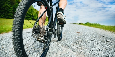 Nahaufnahme eines Fahrradreifens auf einem Schotterweg unter blauem Himmel.