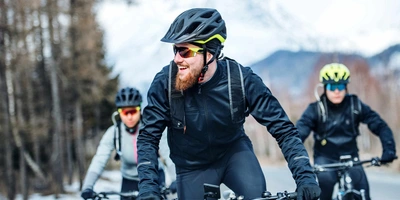 drei Fahrradfahrer mit Helm fahren im Winter auf Straße.