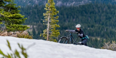 Frau schiebt Mountainbike verschneiten Berg hoch.