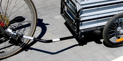 Lerne hier Schritt-für-Schritt, wie du deine Fahrradanhänger montieren kannst! Fahrradanhänger mit Verbindung zu einem Fahrrad auf Pflastersteinen.