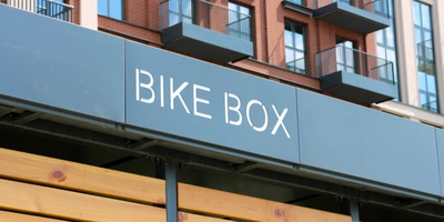 Schild mit der Aufschrift "BIKE BOX" an einer modernen Gebäude-Fassade.