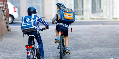 zwei Kinder fahren mit Helm und Rucksack zur Schule