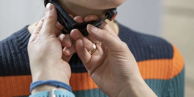 Die Riemen sollten den Hals nicht einengen. Eine Person überprüft bei einer Fahrradhelmträgerin, ob die Riemen den Hals nicht einengen.