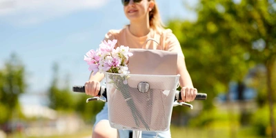 Frau fährt auf Rad mit Fahrradkorb durch eine sonnige Landschaft
