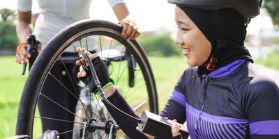 Frau kniet neben einem Fahrrad und Pumpt mit einer Fahrradpumpe den Reifen auf
