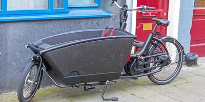 Schwarzes Lastenrad mit großer Transportbox im vorderen Teil steht vor einer Hauswand.