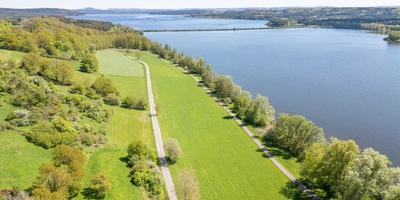 Entdecke den Fränkischen Wasserradweg Luftaufnahme eines Flusses, umgeben von grünen Wiesen und Bäumen.