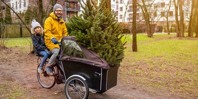 Ein Lastenrad eignet sich hervorragend um den Weihnachtsbaum mit der Familie abzuholen. Mann fährt mit Tochter und Weihnachtsbaum auf Lastenrad