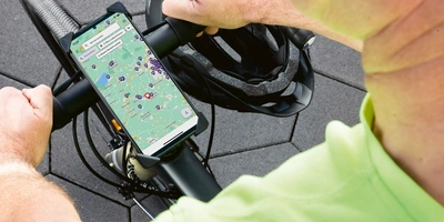 Eine Hand mit einem Smartphone auf einem Fahrradlenker, im Hintergrund ein Helm.