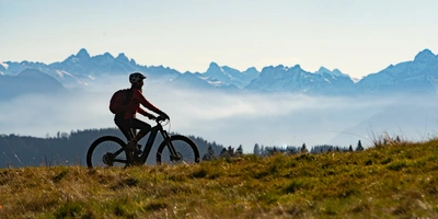 Frau fährt auf einem E-Bike in den Bergen über eine Wiese