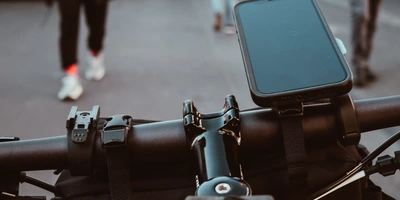 Blick auf den Lenker eines Fahrrads mit einem Smartphonehalter und Fußgängern im Hintergrund.