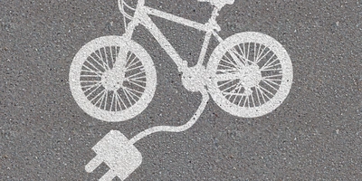 Weißes E-Bike-Symbol auf grauem Asphalt mit einem Steckdosenanschluss