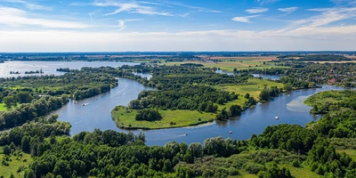 Luftaufnahme eines weitläufigen, grünen Flusslandschaft mit klaren blauen Himmel.