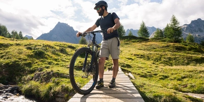 Junger Mann steht auf einer Holzbrücke in der Natur mit einem Fahrrad