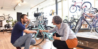 Zwei Personen, ein Kunde und der Verkäufer, befinden sich in einem Fahrradgeschäft. Der Kunde lässt sich vom Fachhändler beraten. 