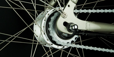 Kettenschaltung oder Nabenschaltung – welche passt zu dir? Detailansicht eines Fahrradnaben mit Speichen und Kette auf schwarzem Hintergrund.