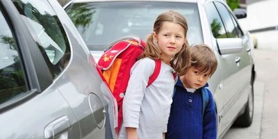 zwei Kinder zwischen Autos schauen vorsichtig auf die Straße
