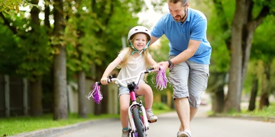 Mann schiebt Kind auf Fahrrad an.