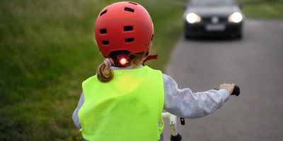 Ein Kind mit rotem Helm und reflektierender Weste fährt mit dem Fahrrad auf der Straße.