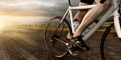 Weißes Rennrad auf einer Straße, von dessen Fahrer Beine und Schuhe auf den Pedalen sichtbar sind. 