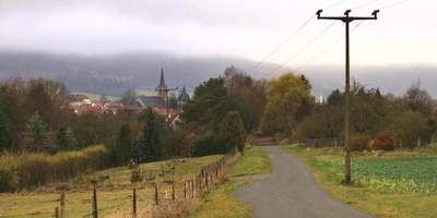 Entdecke den Leine-Radweg Landschaft mit einer kurvigen Straße, herbstlichen Bäumen und einem Dorf im Hintergrund.