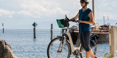 Das Lemmo One gewann den Design & Innovation Award 2023. Frau mit Helm steht neben Fahrrad an einem See.